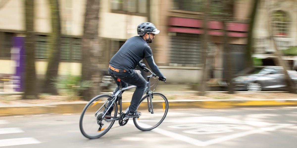 Adult male cycling on city street with helmet, promoting urban mobility.