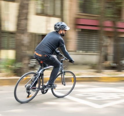 Adult male cycling on city street with helmet, promoting urban mobility.