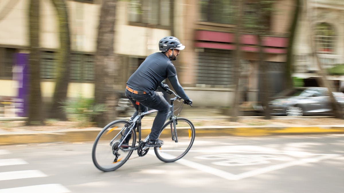 Adult male cycling on city street with helmet, promoting urban mobility.