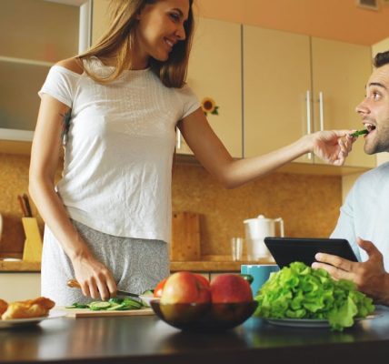 Attractive couple chatting in the kitchen early morning. Beautiful woman feed her husband while cooking breakfast at home